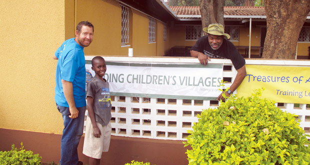 Hikers Ryan Shankles, left, and Jarrot Stanford put up their ministry banner with the help of their young friend Samuel. Shankles and Stanford hiked Mount Kilimanjaro to raise money for an orphanage operated by Treasures of Africa.